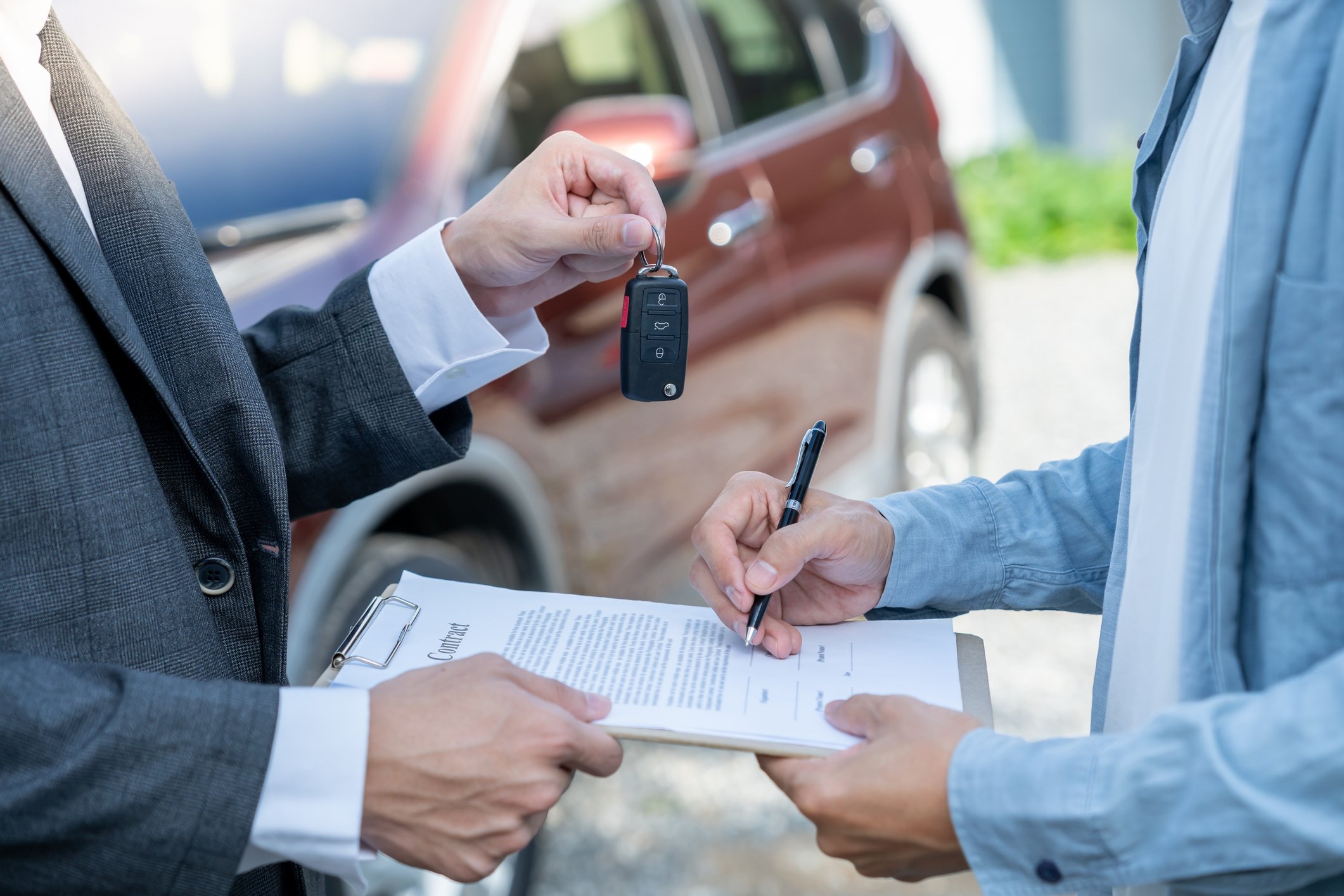 Dealer handing over contract and car keys to new owner to sign